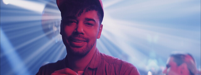 Young man enjoying nightlife at a vibrant party while surrounded by colorful lights and dancing people in an energetic venue