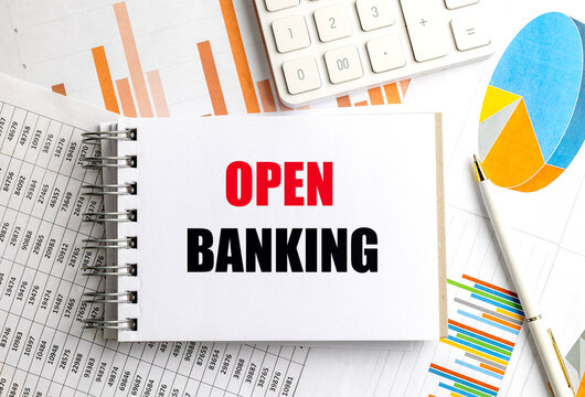 Open banking phrase on spiral notebook with financial charts, pen, and calculator on desk