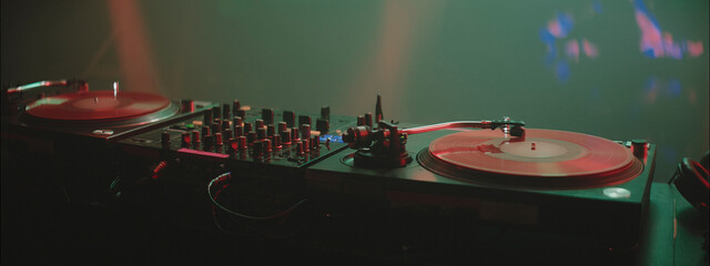 DJ setup with turntables and mixer illuminated by colorful lights during a music event