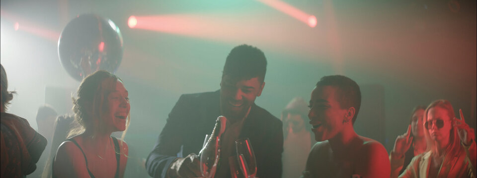 People celebrating at a lively party with dancing, drinks, and vibrant lights during a fun night out