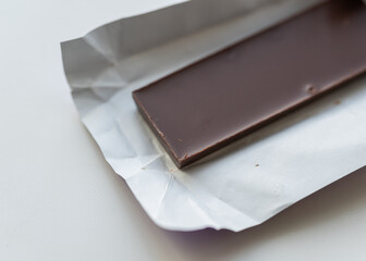 Close-up shot of a smooth dark chocolate bar partially unwrapped in white foil on a clean white background.