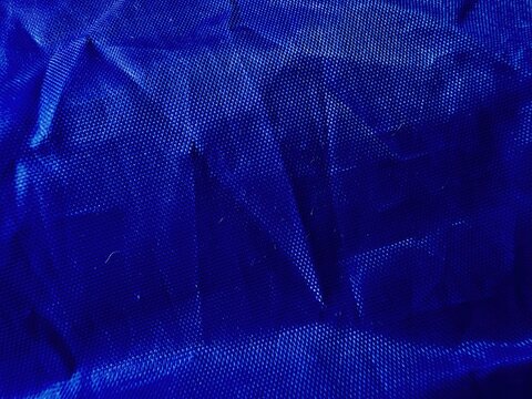 crumpled dark blue textured fabric close-up with wrinkled folds and grid pattern on light background
