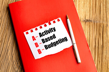 Concept of activity-based budgeting written on torn paper on red notebook with pen on wooden desk