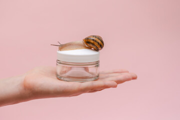 Glass cosmetics bottle with snail in woman's hand. Mockup for brand. Skin care product, spa,...