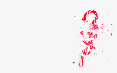 A candy cane shattered into several pieces on a bright white background. The fragments are festive red and white, typical for the holiday season, celebrating winter traditions.