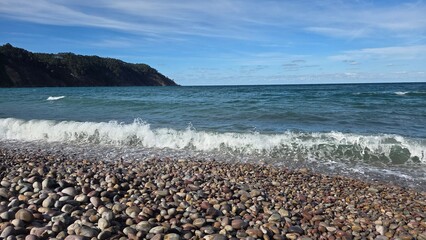 Serene ocean view with rocky shoreline and distant coastal cliffs under clear blue sky. Horizontal banner. Copy space. Travel, vacation concept