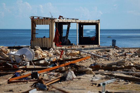 Dilapidated wooden shack and debris on a rocky shoreline with the ocean in the background