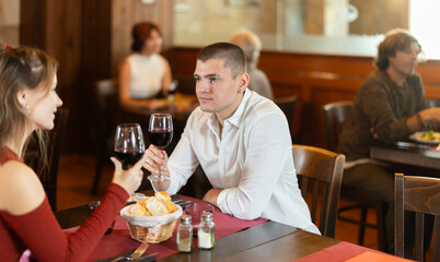 Happy young couple man and woman eating drinking and talking in restaurant