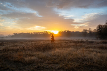 Woman Wearing Cowboy Hat Riding Horse and Looking Off At Golden Hour of Sunset With Cloudy Sky
