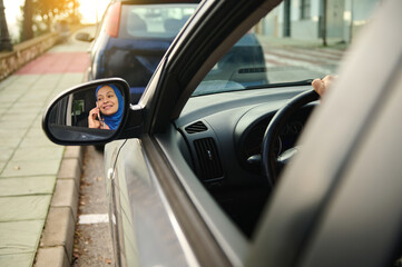 Hijab-Clad Woman on Phone Inside Car, Reflected in Side Mirror on European Street