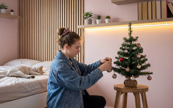 Girl decorating small Christmas tree in bedroom