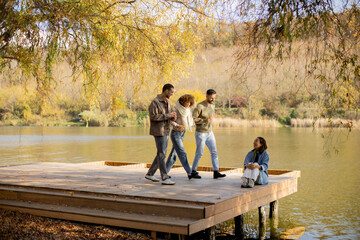 Friends enjoying a sunny day by the lake on a wooden deck surrounded by vibrant autumn trees
