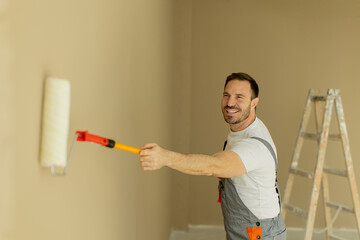 Man painting a wall with a roller while smiling in a home renovation project
