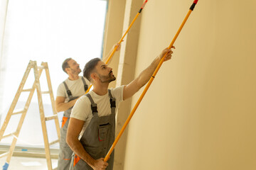 Workers apply fresh paint on a wall in a modern interior setting during daylight © BGStock72