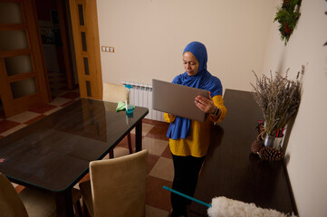 Muslim Woman In Hijab Working On Laptop At Home In Modern European Setting