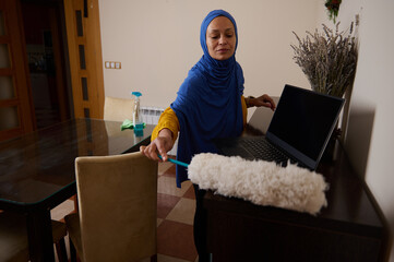Hijab-Wearing Woman Cleaning Office Desk With Laptop At Home