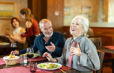Happy elderly couple man and woman eating drinking and talking in restaurant