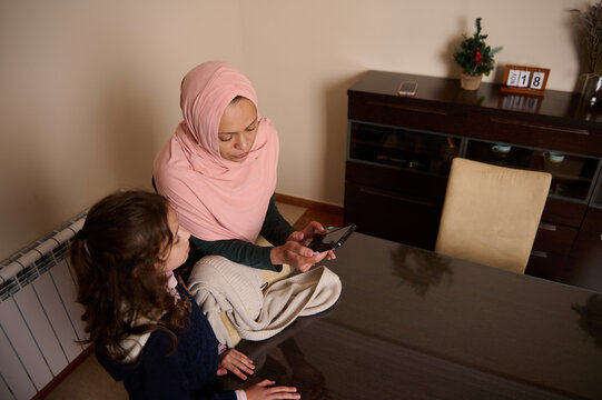 Mother in Pink Hijab Shares Phone Moment with Daughter at Cozy Modern Dining Table