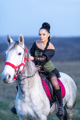 Beautiful young woman in medieval dress with white horse on the field. 