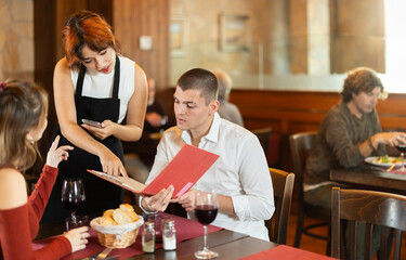 Attentive young waitress taking order from young couple during relaxed dinner in comfortable restaurant setting