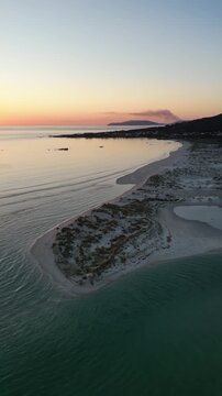 Aerial view of the beach meeting the sea under the sunset sky, with contrasting textures of sand and water, Carnota, A Coruna, Spain.