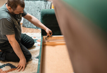 Man disassembling sofa furniture mechanism at home using furniture wrench. DIY Assembling Furniture concept.