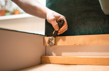 Man disassembling sofa furniture mechanism at home using furniture wrench. DIY Assembling Furniture concept.