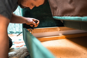 Man disassembling sofa furniture mechanism at home using furniture wrench. DIY Assembling Furniture concept.