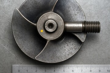 Metal impeller with threaded shaft measured by steel ruler.