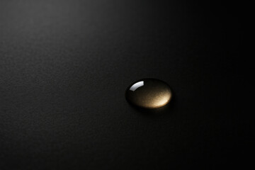 A single golden drop on a dark matte surface. Space for text.