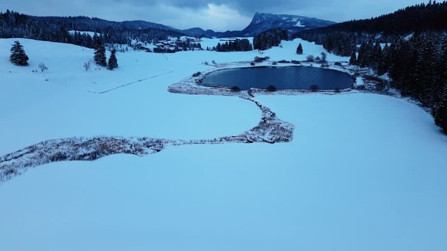 Aerial view of Lake Ter surrounded by snow covered fields and hills, creating a serene winter landscape, Le Lieu, Vaud, Switzerland.