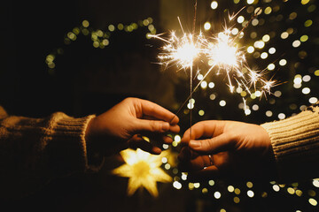 Happy New Year! Burning sparklers in hands on background of christmas tree golden lights bokeh at night. Glowing fireworks in couple hands, new year eve holiday celebration