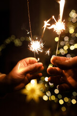 Happy New Year! Burning sparklers in hands on background of christmas tree golden lights bokeh at night. Glowing fireworks in couple hands, new year eve holiday celebration