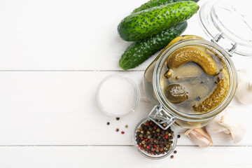 Pickled cucumbers in jar and ingredients on white wooden table, flat lay. Space for text