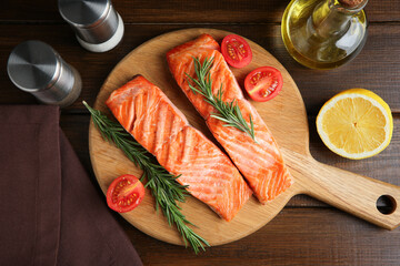 Pieces of tasty grilled salmon, rosemary, tomatoes and spices on wooden table, flat lay