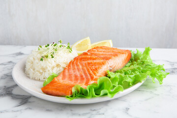 Piece of tasty grilled salmon, lemon, lettuce, rice and microgreens on light marble table against grey background, closeup
