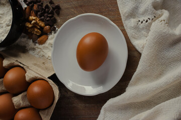 Tasty ingredients on a rustic wooden table, brown eggs in a white dish, flour, chocolate chips, and almonds and walnuts for preparing homemade desserts and cooking healthily.