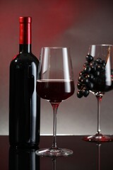 Red wine in glass, bottle and grapes on black table against color background