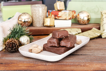 Delicious Dubai chocolate bars and whole pistachios on a rustic wooden table, with Christmas decorations symbolizing sweets and the preparation of gourmet desserts for Christmas