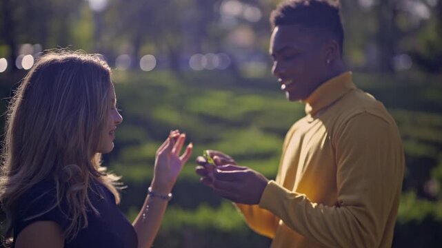 A happy diverse couple shares an intimate moment, discussing a small plant in a sun-drenched park. Their genuine smiles reflect their strong connection and joy during this pleasant day. - Powered by Adobe
