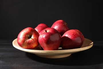 Ripe red apples on wooden table against black background, closeup