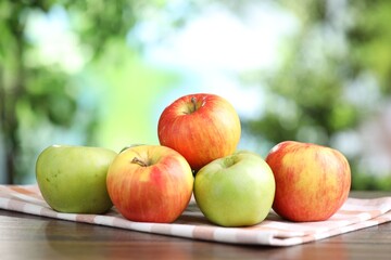 Fresh red and green apples on wooden table against blurred green background, closeup