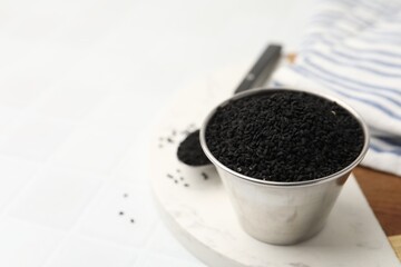 Aromatic black caraway in bowl and spoon on white table, closeup. Space for text
