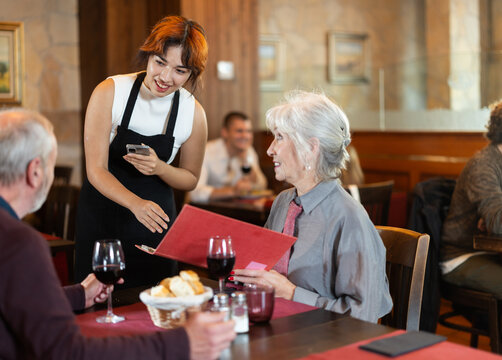 Filipino girl listen to restaurant couple of customer, write down order items in phone note, record order dish name in mobile application. Waitress of public catering answer customers question