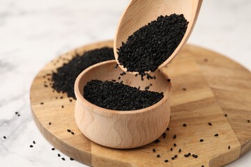 Pouring aromatic black caraway into bowl at white marble table, closeup