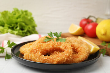 Deep fried squid rings with parsley and lemon slice on white tiled table, closeup