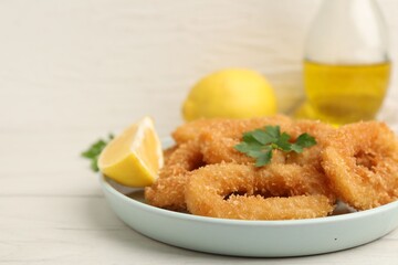 Deep fried squid rings with parsley and lemon slice on white table, closeup. Space for text