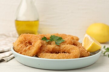Deep fried squid rings with parsley and lemon slice on white table, closeup. Space for text