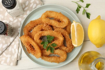 Deep fried squid rings with parsley and lemon slice on white table, flat lay