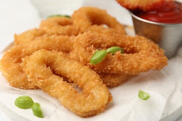 Deep fried squid rings with basil and ketchup on white table, closeup